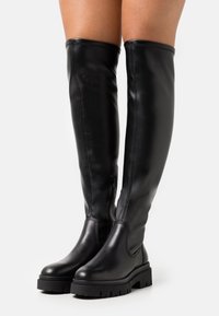 Botas negras hasta la rodilla, hechas de cuero suave, con una suela texturizada gruesa, una silueta esbelta y un detalle de cremallera lateral.