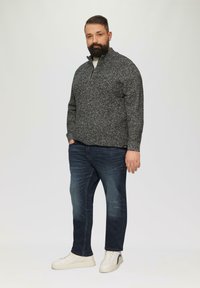 Grau und schwarz gesprenkelter Reißverschluss-Pullover, lockere Passform, kombiniert mit dunkelblauen Jeans und weißen Turnschuhen mit grauen Akzenten. Glatte Textur.