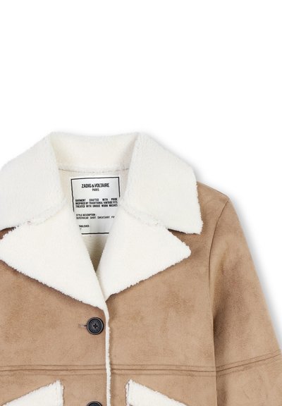 Bruine suède jas met een witte schapenvacht kraag, voorzien van zwarte knopen en een label met informatie over materiaal en verzorgingsinstructies.