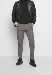 Svart läderbomberjacka, åtsittande svart polotröja, ljusgrå skräddarsydd byxor och svarta snörskor. Släta texturer och neutrala toner.