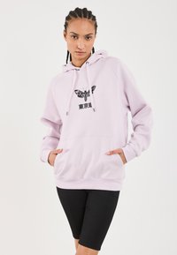Lys rosa hettegenser med frontlomme, svart sommerfugl-grafikk og japansk tekst. Har snor i hetten og ribbede mansjetter. Svart shorts.