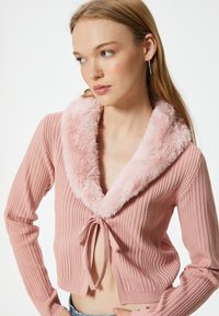 Rosa, kürzer geschnittenes Sweatshirt mit gerippter Textur, ausgestattet mit einem flauschigen Kragen und einem Frontknotenverschluss. Lange Ärmel und ein weiches, gemütliches Erscheinungsbild.