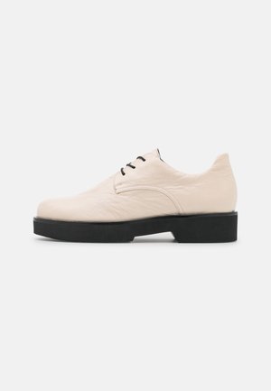 Chaussure Oxford en cuir crème à lacets, avec bout arrondi et semelle épaisse noire, vue de profil orientée vers la gauche sur fond blanc.