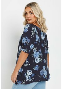 Blusa floral de tela azul marino con mangas cortas abullonadas. Presenta grandes patrones de flores azules y blancas y un corte holgado.