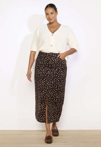 Rjava cvetlična midi krila z razporkom spredaj, elastičnim pasom in lahkotnim materialom, v kombinaciji s kremnim cardiganom na gumb in nepremočljivimi čevlji.