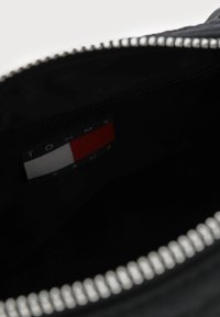 Interno nero di una borsa con una cerniera argentata. Visibile un'etichetta in tessuto con sezioni rosse, bianche e blu etichettata "TOMMY JEANS."