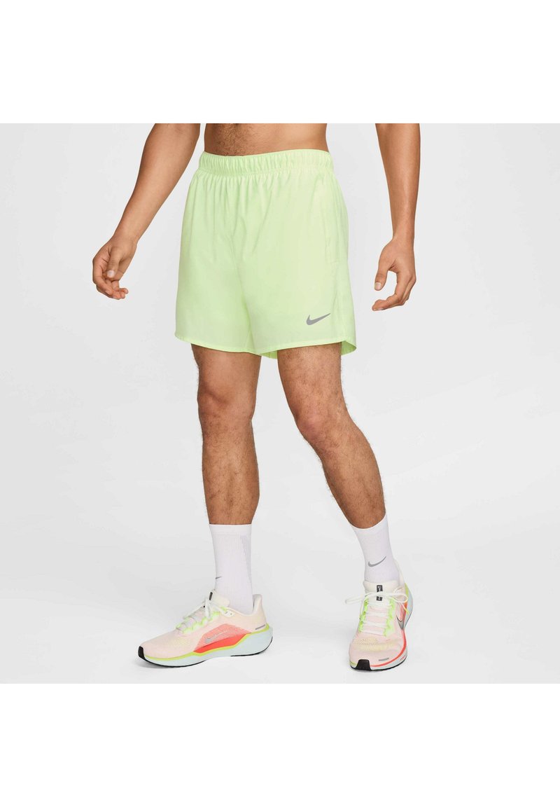 Vihreät neonväriset urheilushortsit, joissa on joustava vyötärö. Mallissa on harmaa Nike-logo. Malli on yhdistänyt shortsit pastellivärisiin juoksukenkiin ja valkoisiin sukkiin.