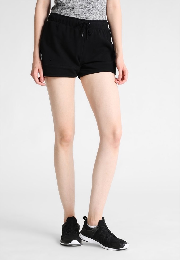 Svarta atletiska shorts med elastisk midjeband och dragsko. Slät textur och åtsittande design, kombinerade med svarta sneakers.