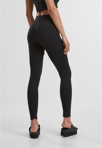 Leggings neri realizzati in materiale elastico, caratterizzati da una vita alta e un design aderente. Indossati con sandali neri con plateau.