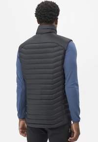 Gilet matelassé noir avec un design matelassé diagonal, col montant et tissu léger, porté par-dessus une chemise à manches longues bleue.