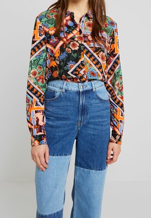 Femme portant une chemise à manches longues colorée, à imprimé floral et animal, rentrée dans un jean bleu bicolore taille haute.