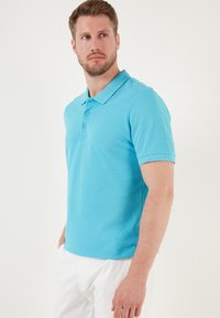 Polo de color azul claro, fabricado en algodón suave, con collar clásico, tapeta de tres botones y mangas cortas. Diseño liso, sin patrones.