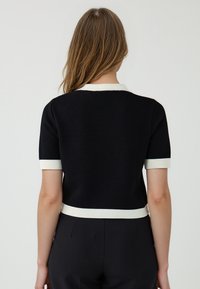 Top corto a maniche corte in maglia nera con colletto e polsini a coste bianchi, caratterizzato da un design aderente e una texture liscia, visto da dietro.