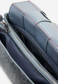 Borsa in tessuto grigia con dettagli in pelle blu liscia, caratterizzata da numerosi scomparti con cerniera e cuciture rosse a contrasto.