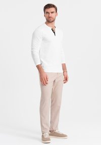 Witte long-sleeve henley shirt met een zwarte bijpassende knopenlijst, beige broek en lichtgekleurde sneakers, met een slim fit en een gladde textuur.