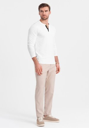 Langärmliges weißes Henley-Shirt mit schwarzer Knopfleiste, beigen Hosen und hellen Sneakers, mit schlankem Schnitt und glatter Textur.