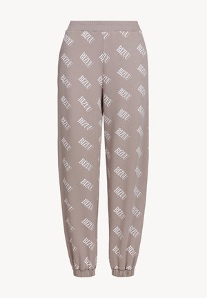 Jasnobrązowe dresy z miękkiego materiału mają nadruk z logo "BIZUU" w kolorze białym na całej powierzchni, elastyczny pasek w talii oraz ściągacze przy kostkach.