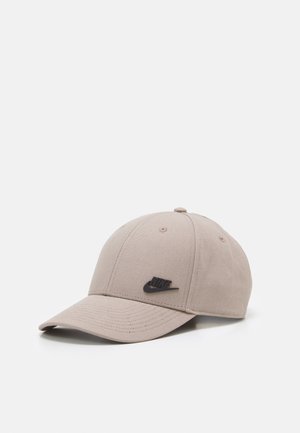 Casquette de baseball beige Nike avec une visière courbée et un logo noir sur le devant, présentée sur un fond blanc.