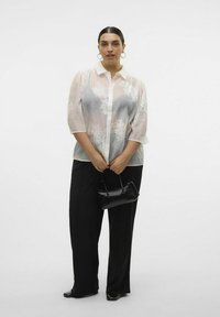 Leichte, transparente Button-Up-Bluse mit floralem Stickerei, kombiniert mit schwarzen weiten Hosen und einer kleinen schwarzen Handtasche.
