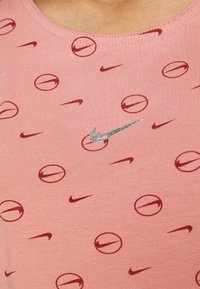 Rosa bomullstopp med ett upprepat mönster av röda Nike-logotyper och cirkulära mönster, med ett silverfärgat Nike-emblem i mitten.