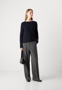 Maglione a coste di colore navy abbinato a pantaloni grigi a gamba larga. Gli accessori includono una piccola borsa nera e scarpe basse marroni.