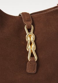 Brown suede bag with a gold chain link accent, featuring a leather strap and stitched detailing. Texture is soft and matte.