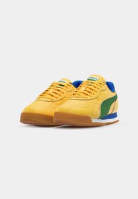 Κίτρινες αθλητικές παπούτσια με πράσινες και μπλε λεπτο�μέρειες, κατασκευασμένα από υλικό με υφή, διαθέτοντας μαλακό περίβλημα στον αστράγαλο, λευκή ενδιάμεση σόλα και καουτσούκ σόλα.