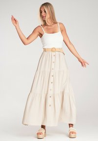 Helle beige Maxi-Rock mit gestuften Design, Vorderknöpfen und einem gewebten Gürtel. Kombiniert mit einem weißen Tanktop und Plateausandalen.