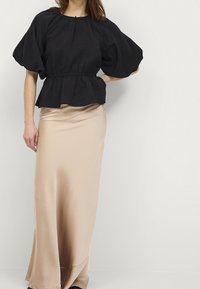 Black textured blouse with puff sleeves, cinched waist, and a keyhole back, paired with a long, smooth, beige satin skirt.