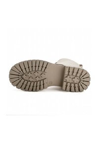 Suola di scarpa in gomma beige con scanalature profonde e superficie testurizzata. Presenta righe orizzontali e un'impronta del logo centrale.