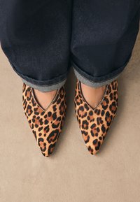 Les ballerines pointues à imprimé léopard présentent une texture douce avec une découpe basse sur les côtés, complétant un jean en denim foncé roulé à ourlet rayé.