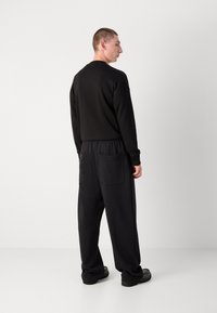Schwarzes Sweatshirt mit Rundhalsausschnitt, kombiniert mit schwarzen, locker sitzenden Hosen mit zwei großen Gesäßtaschen und elastischem Bund.