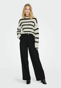 Gestreifter Pullover in Beige und Schwarz, kombiniert mit hochtaillierten schwarzen Hosen. Der Pullover hat eine lockere Passform und eine gerippte Textur.