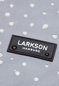Superficie grigia con gocce testurizzate; un'etichetta in pelle nera con lettere bianche riporta la scritta "LARKSON HAMBURG." Presenta un design elegante e moderno.