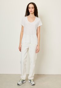 Balta, lengva marškinėlių su apvaliu iškirpimu, derinama su šviesiai baltais tiesaus kirpimo džinsais ir raštuotais sportiniais bateliais.