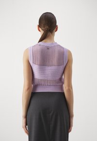 Lilas neulepeliton toppi, jossa on avoin kudontamalli ja ribbireuna, kerroksittain tummanharmaan kynähameen päällä. Takakatsaus näkyvissä.