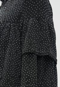 Svart tyg med små vita prickar, som har ett lager av volangdetalj på ärmen eller fållen.