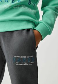 Mintgrön sweatshirt med strukturerad tyg, med djärva blå bokstäver. Grå sweatpants med broderad branding och en slät yta.