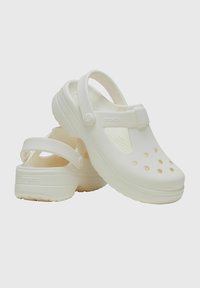 Białe gumowe klapki z perforowanym wzorem, regulowanym paskiem na pięcie i grubą podeszwą. Posiadają logo "CROCS" po boku.