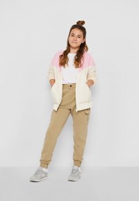 Lätt, krämfärgad bomberjacka med rosa detaljer, vit t-shirt, beige cargobyxor och grå sneakers med rosa inslag. Avslappnad passform.