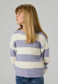 Maglione a righe color lavanda e crema. Tessuto a coste, scollatura rotonda e vestibilità ampia. Indossato con jeans in denim con dettagli a forma di cuore.