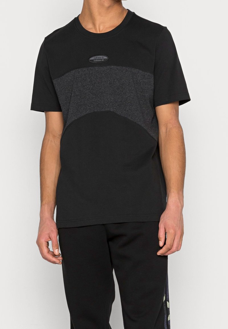 Černé tričko s šedým texturovaným panelem přes hrudník, kulatý výstřih, krátké rukávy, se středovým logem na nášivce.