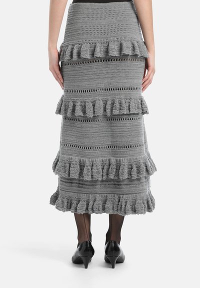 Siva kukičana suknja s slojevitim volanima, otvorenim uzorkom i dugom dužinom. Uparena s crnim cipelama na petu i prozirnim čarapama.