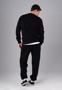 Black sweatshirt with long sleeves, ribbed cuffs, and hem. Paired with black sweatpants and black shoes with white soles and socks.