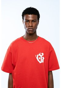 Camiseta de algodón roja con un logo gráfico blanco en el lado izquierdo del pecho, mangas cortas y un corte relajado. Textura suave y diseño sencillo.