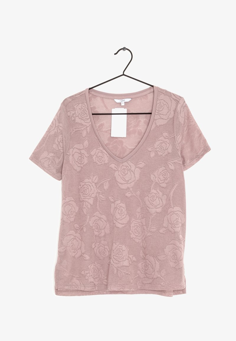 Top rose clair à manches courtes avec col en V et motif de roses, suspendu sur un cintre noir, avec une étiquette de prix blanche attachée au col.