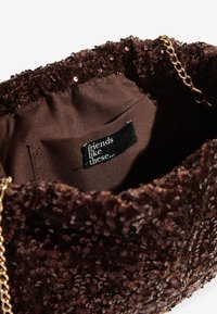 Geantă de mână maro cu paiete, cu partea superioară strânsă și curea de lanț aurie. Interiorul are un căptușeală din material întunecat și o etichetă inscripționată cu "prieteni ca aceștia".