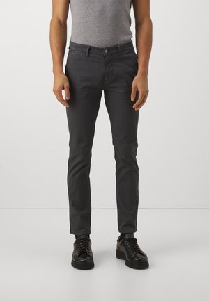Szare bawełniane spodnie o slim fit, z zapięciem na guziki, bocznymi kieszeniami oraz kieszeniami z tyłu, w połączeniu z czarnymi butami na sznurówki.