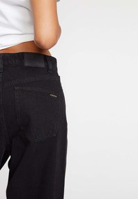 Zwarte denim jeans met een hoge taille, voorzien van een achterzak met een gouden logo-detail en een gestructureerde tailleband.