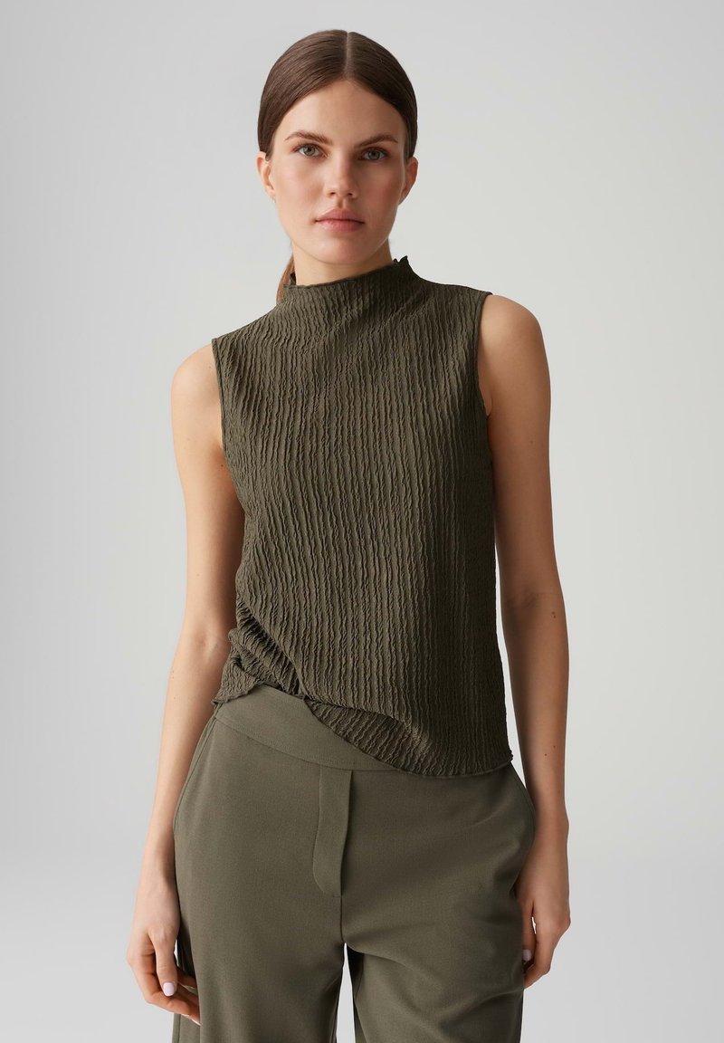 Top senza maniche di colore verde oliva con colletto alto, caratterizzato da un design testurizzato a costine. Abbinato a pantaloni fitted coordinati.